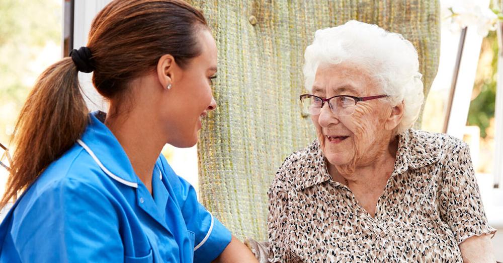 Healthcare worker sitting with a senior woman.