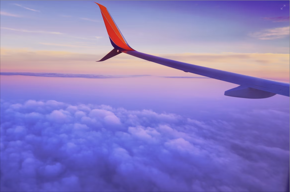 Airplane wing flying over colorful clouds.