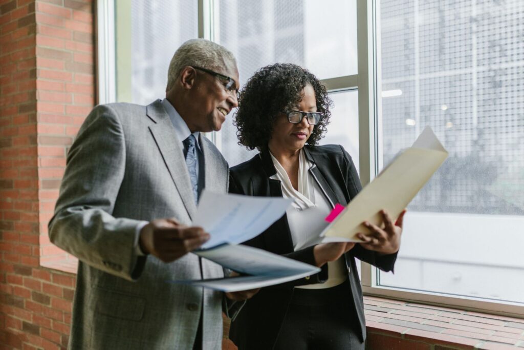 Older man and woman advisors wearing professional attire and glasses reviewing training material that will help guide senior care placement advisors to success. 